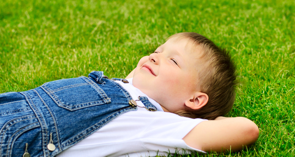 Young boy laying in the green grass.