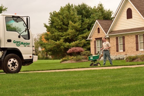 A lawn care professional uses an overseeding machine to spread grass seed across a residential lawn, helping promote thicker, healthier turf.