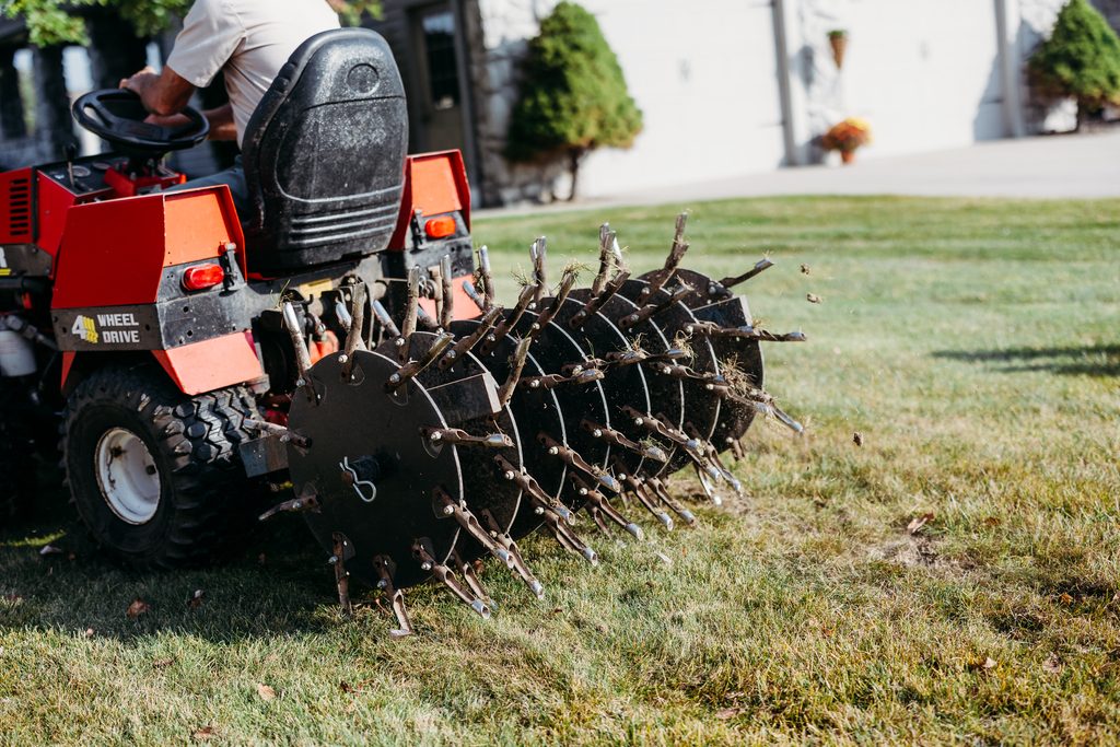 Lawn care professional using a commercial core aerator to aerate a residential lawn and improve soil health.